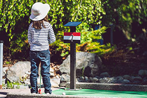 Child wearing a white hat and striped shirt standing at a mini golf tee.