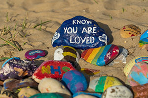 Painted stones on a beach; one has the message: know you are loved.